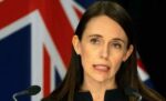 Jacinda Ardern standing in front of a NZ flag